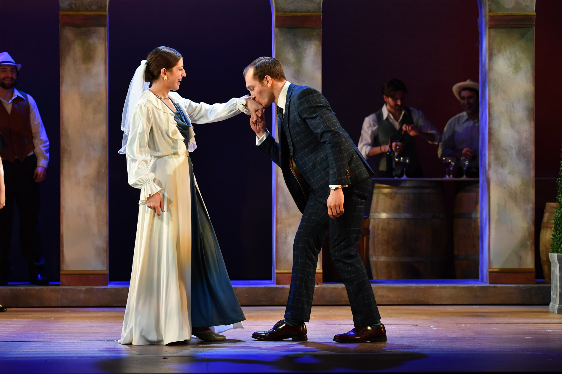 A male and a female opera singer, one wearing a white dress, the other kissing her hand, singing on stage.